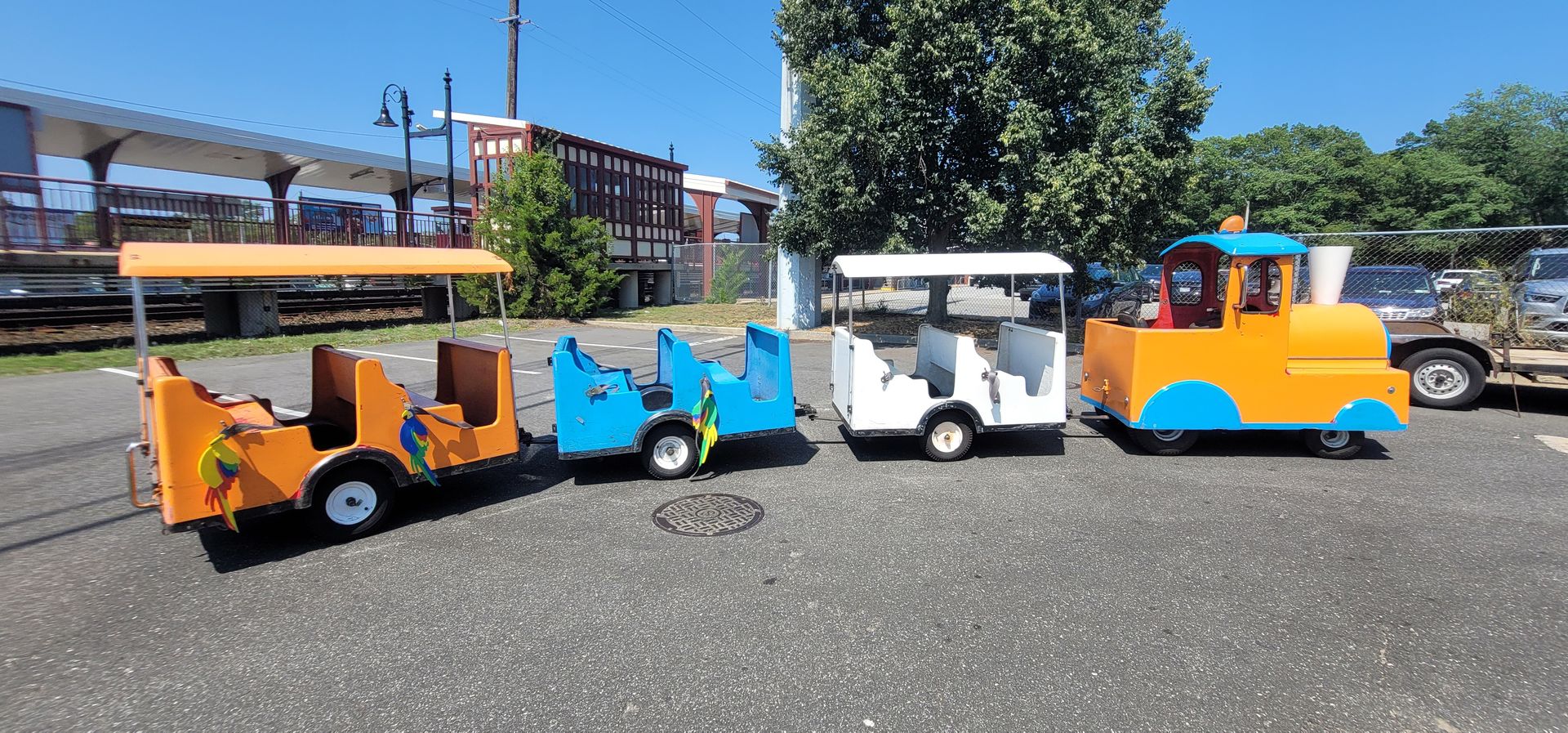 Colorful mini train ride cars lined up outdoors on gravel under a sunny sky
