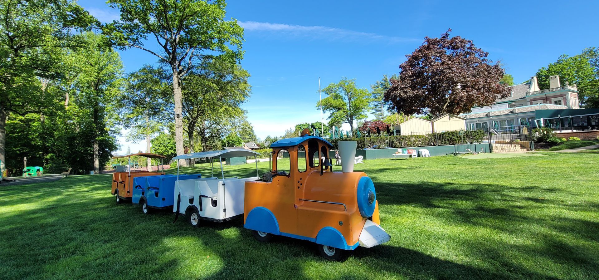 Children riding a yellow miniature train curving through a park on a sunny day