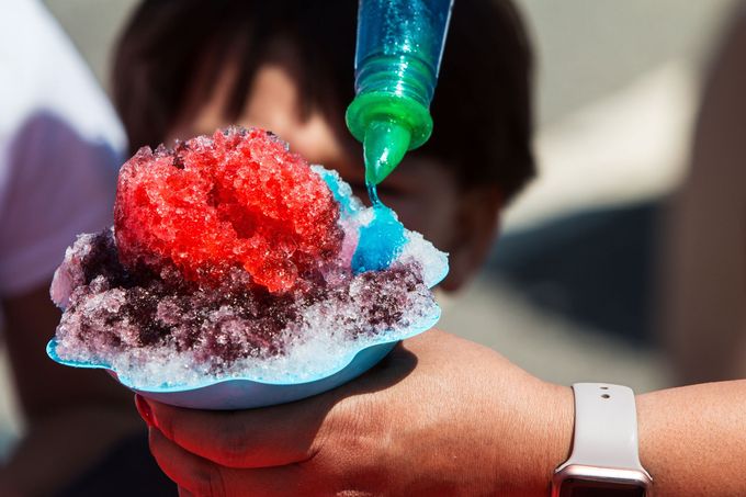 Close-up of shaved ice with red and blue syrup being drizzled into a cup