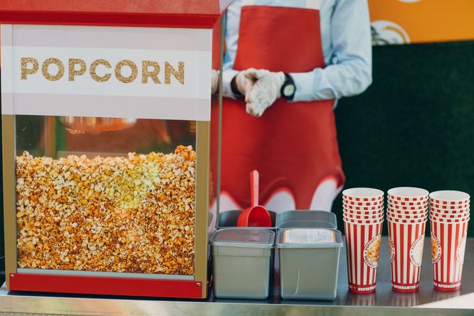 Popcorn machine with freshly popped popcorn, red-and-white cups, and a vendor behind the counter