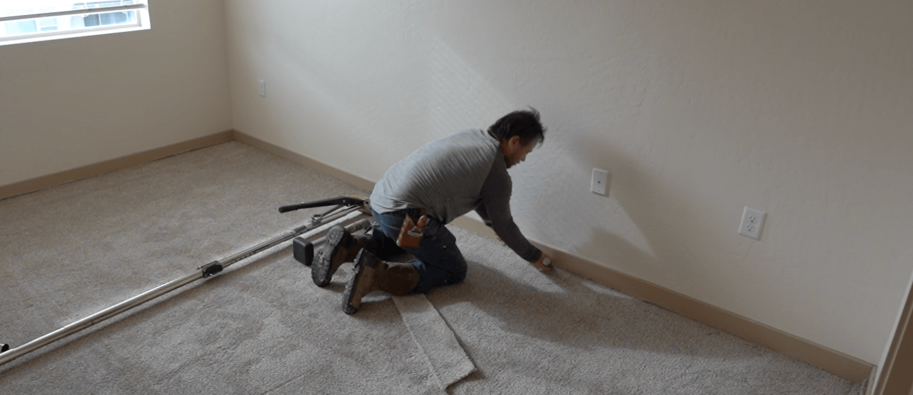 Worker kneeling on carpet, smoothing floor near wall during home renovation