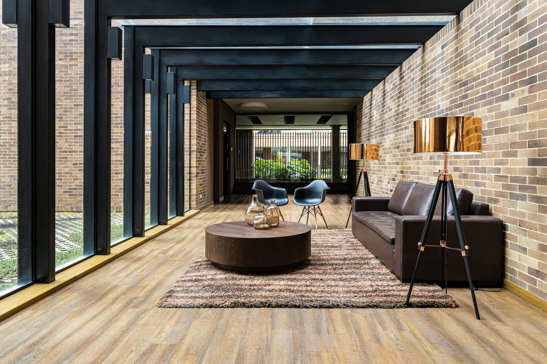 Modern covered patio with wood floor, black beams, sofa, coffee table, rug, and dining area leading to a garden.