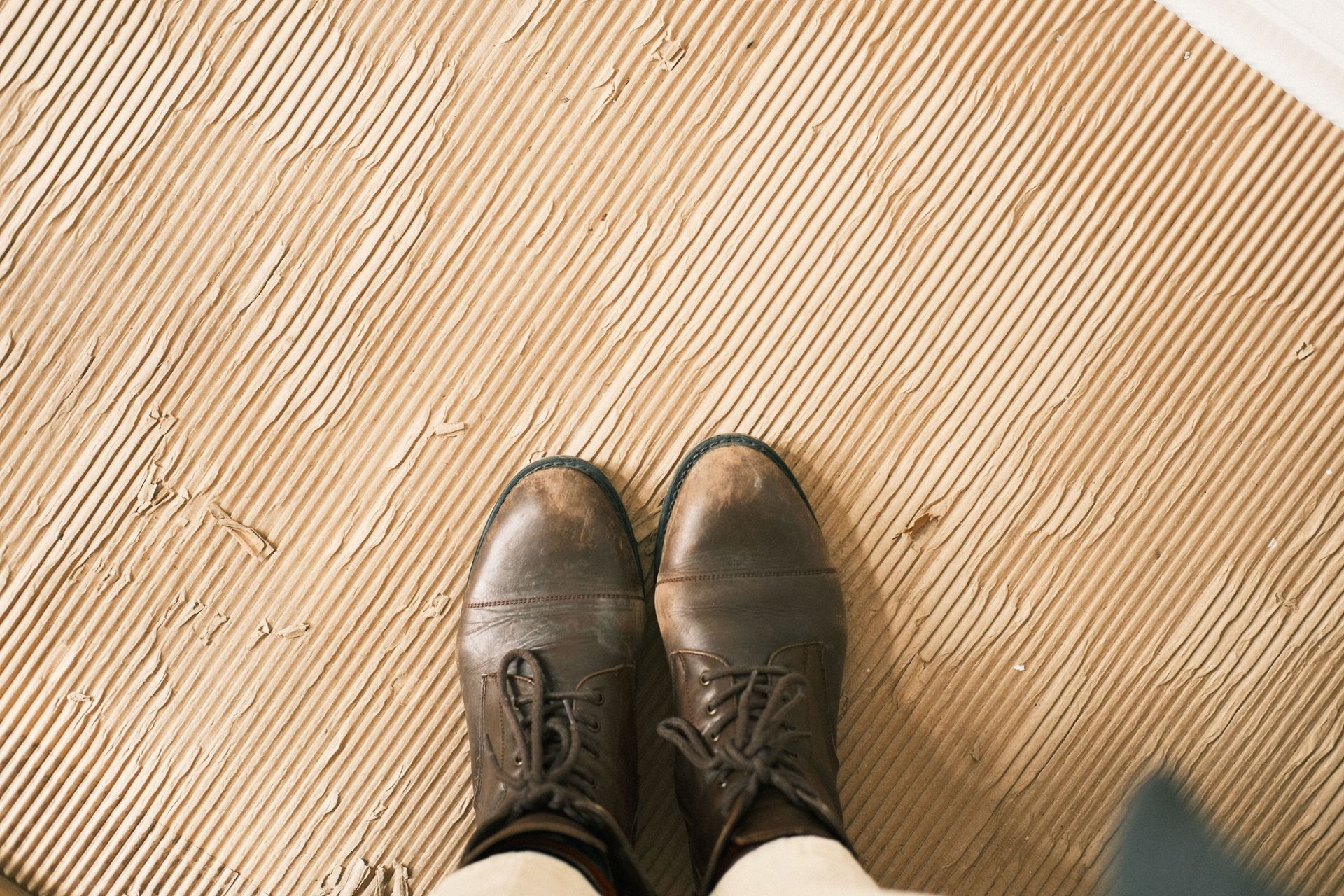 Brown dress shoes standing on a light tan textured floor.