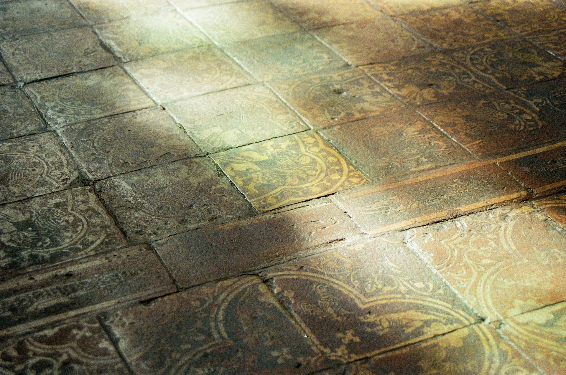 Sunlit stone floor with worn, patterned tiles in earthy green and brown tones