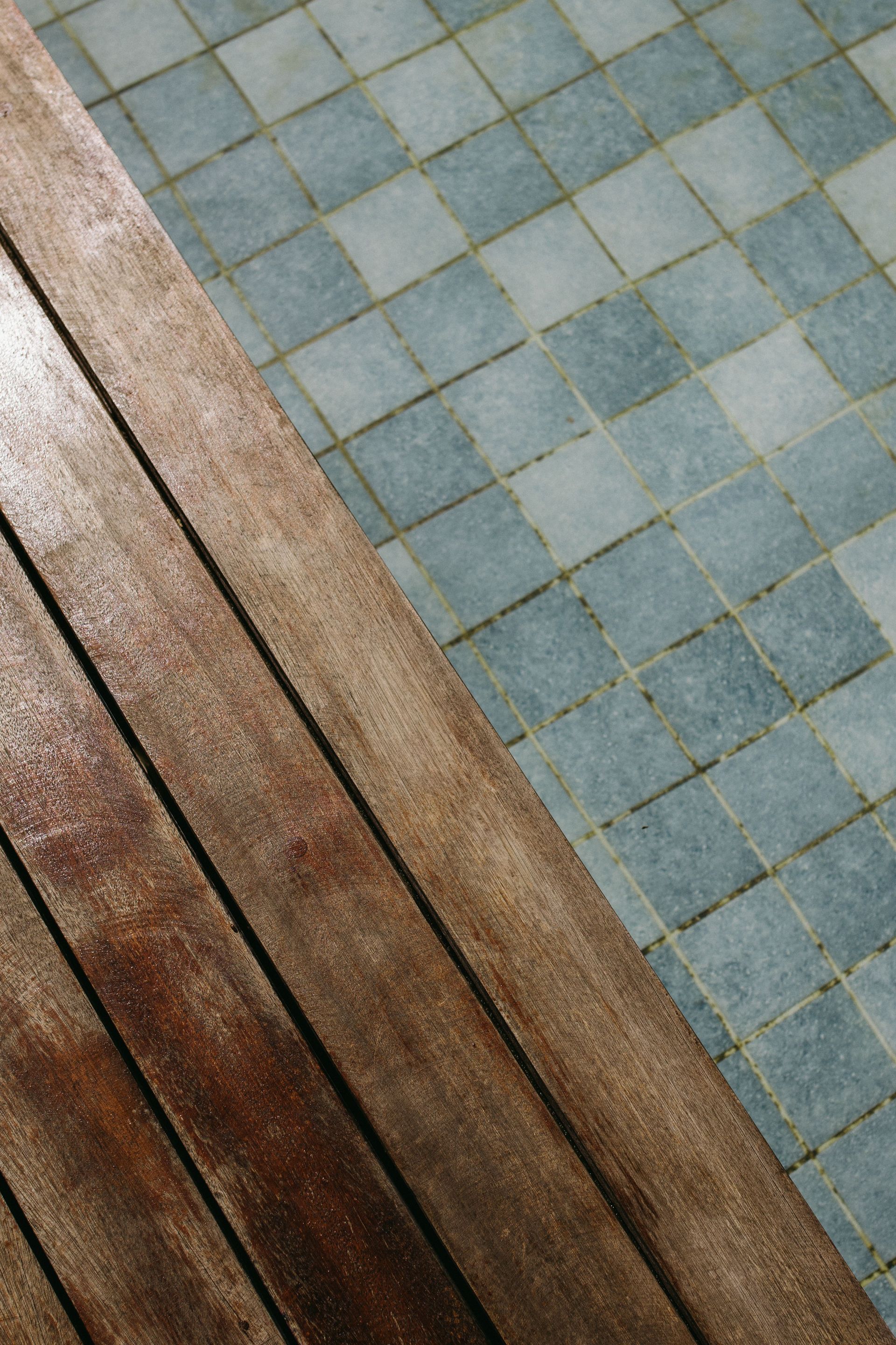 Diagonal view of weathered wooden planks beside a blue-green tiled floor