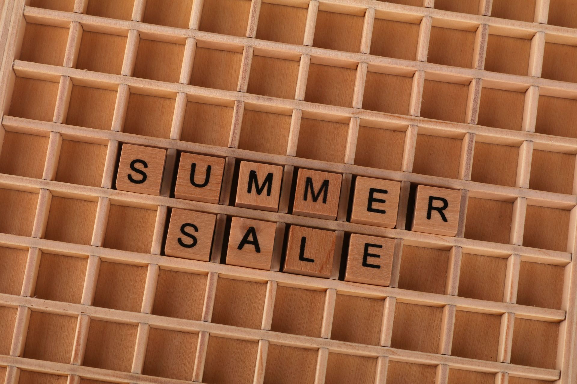 Wooden letter tiles spelling “SUMMER SALE” on a tan lattice background