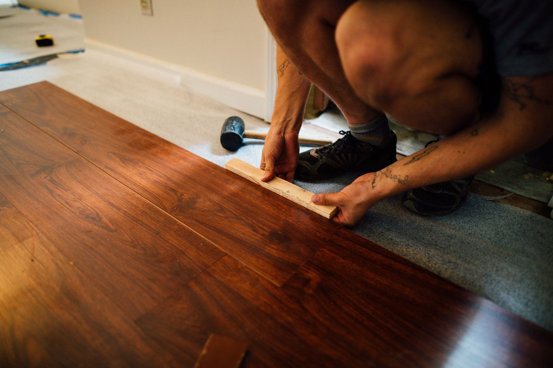Person installing hardwood floor with a measuring tape in a room