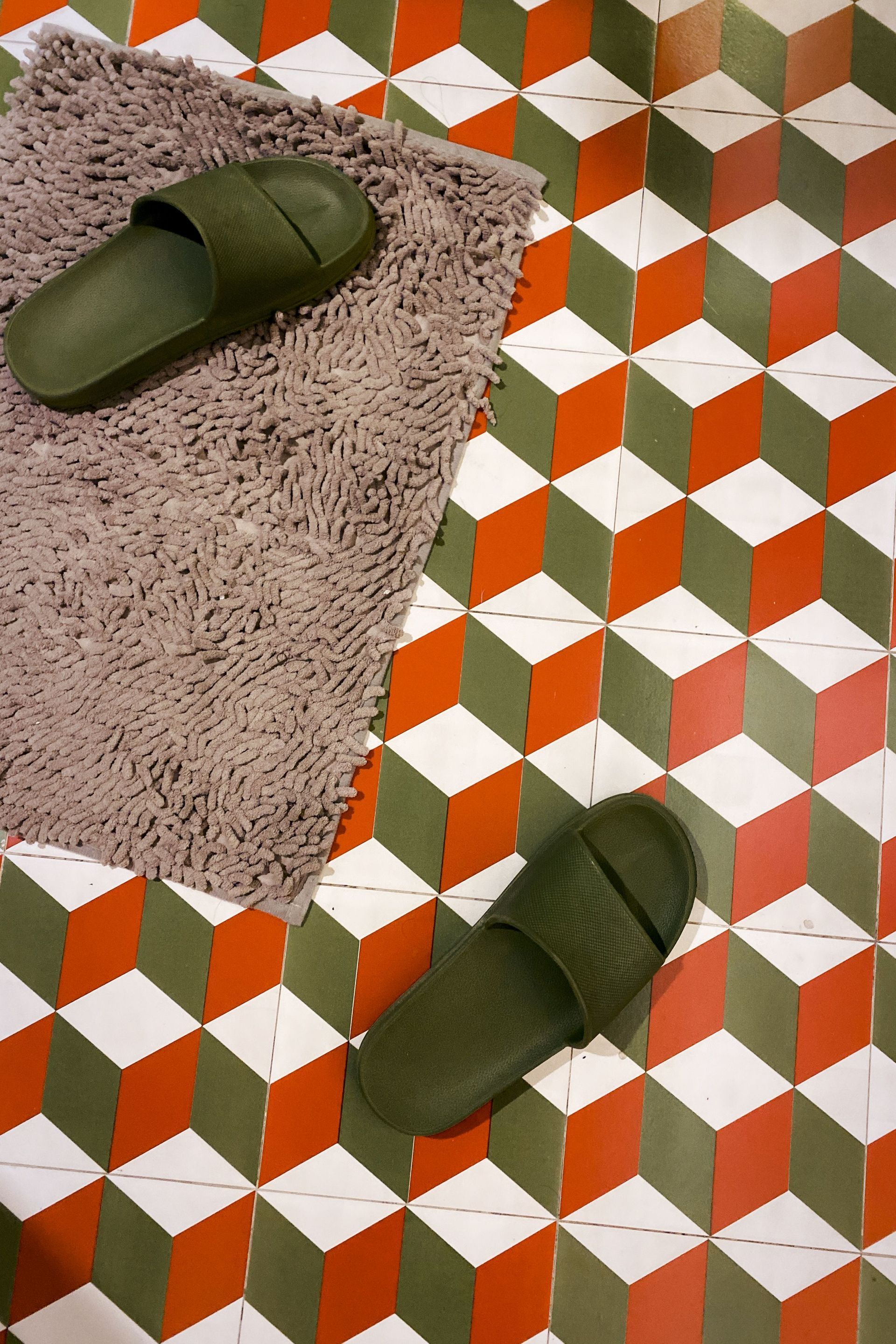Two green slippers on a patterned tile floor beside a beige rug