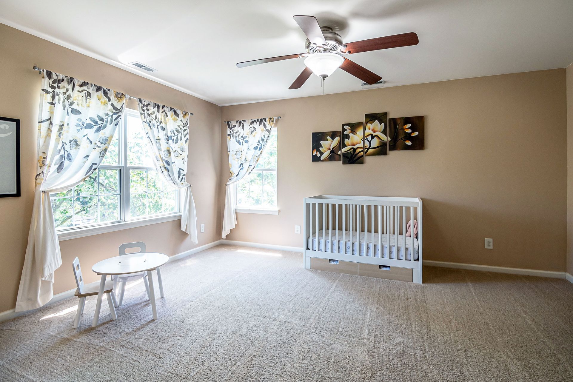 Bright nursery with crib, small table, and large windows with curtains in a carpeted room