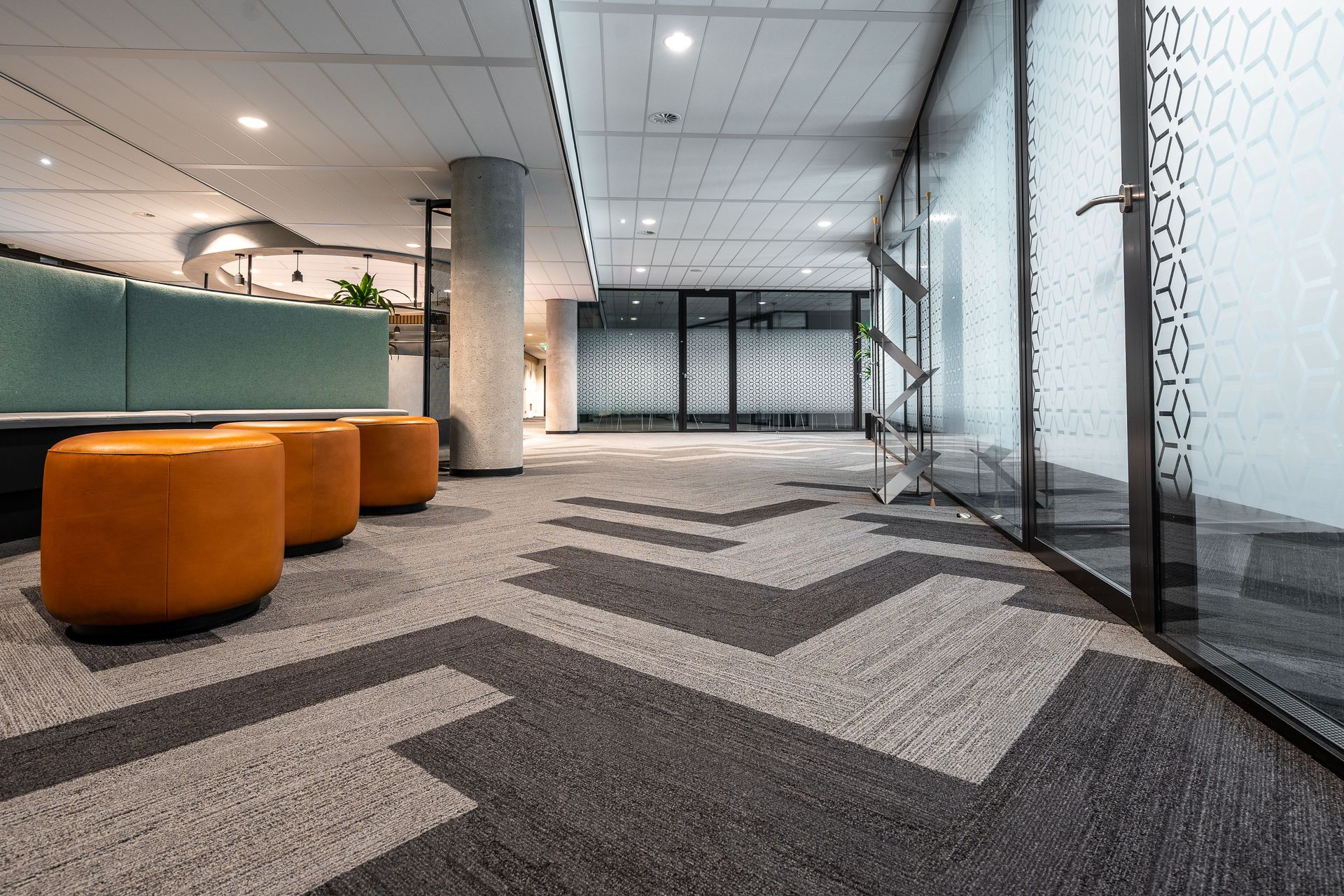 Modern office lounge with orange ottomans, patterned carpet, and glass walls
