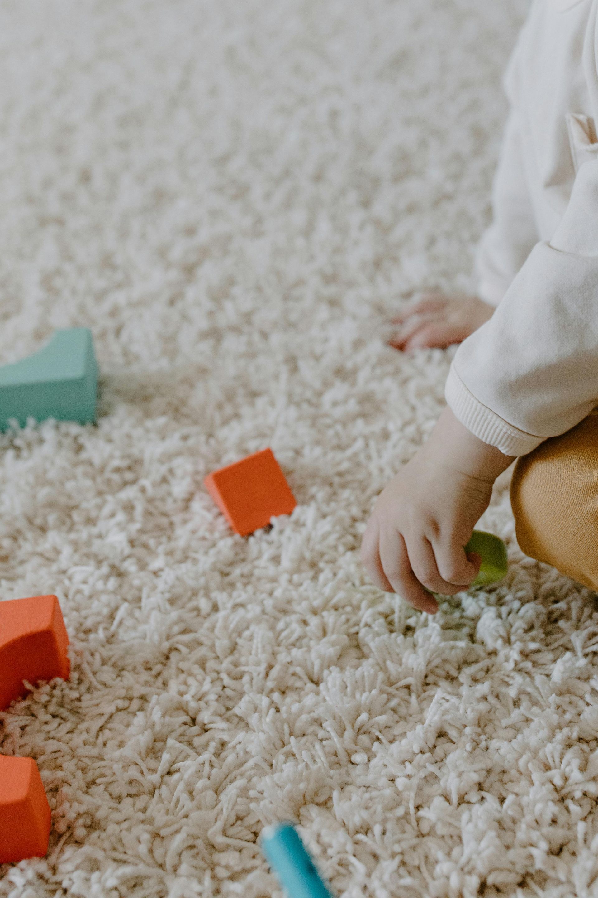 Child’s hand on white shag rug with colorful toy blocks scattered nearby