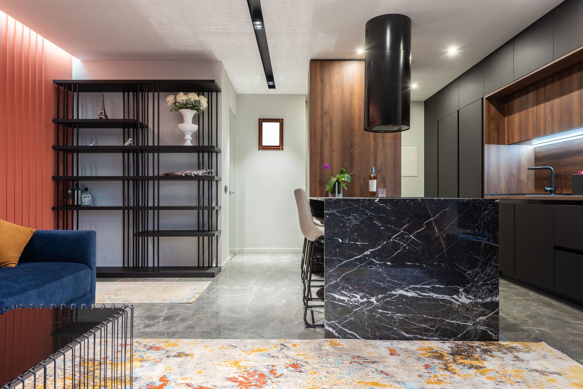 Modern open-plan living room and kitchen with black marble island, shelving, and warm wood accents.