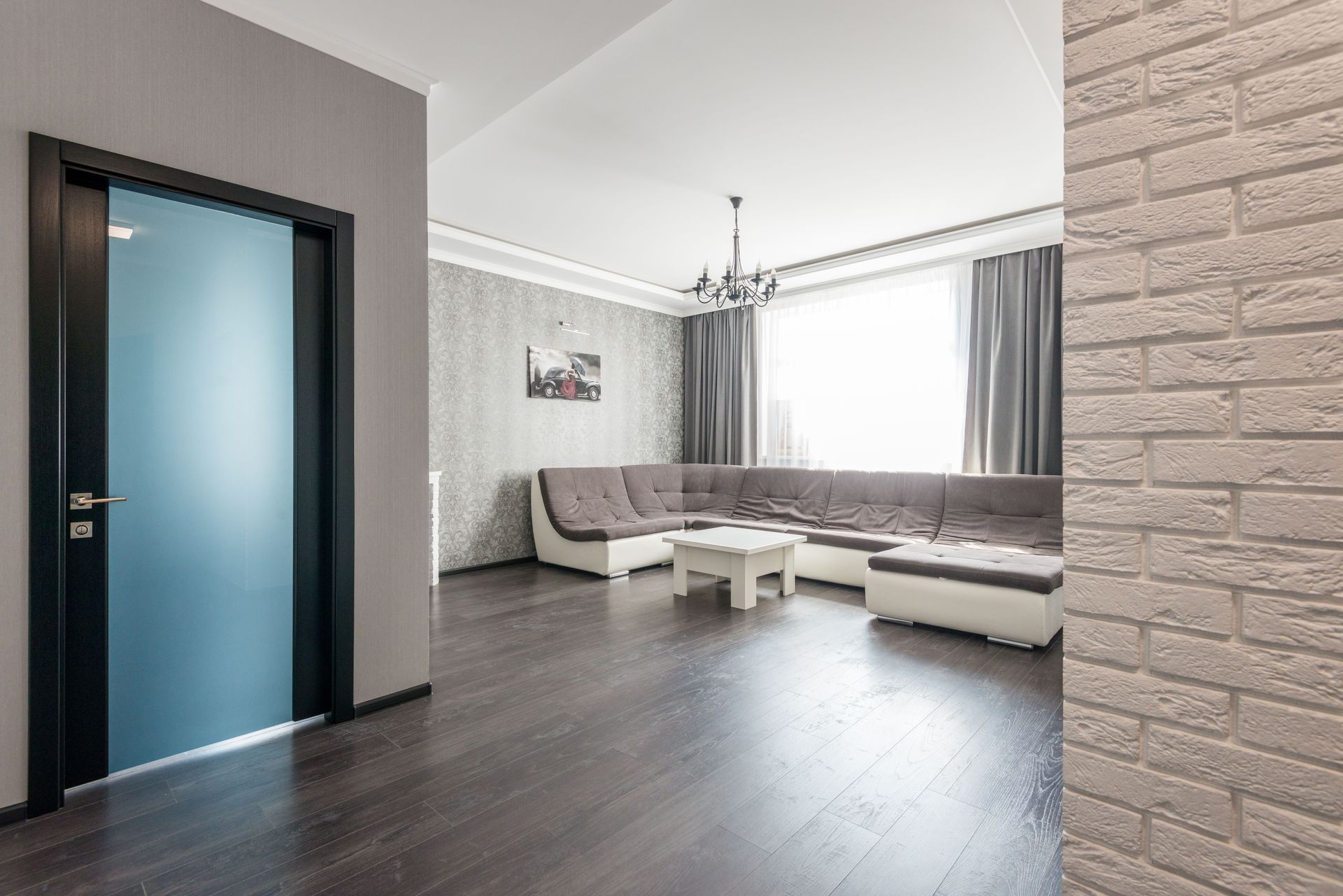 Modern living room with gray sectional sofa, dark wood floor, large window, and frosted glass door
