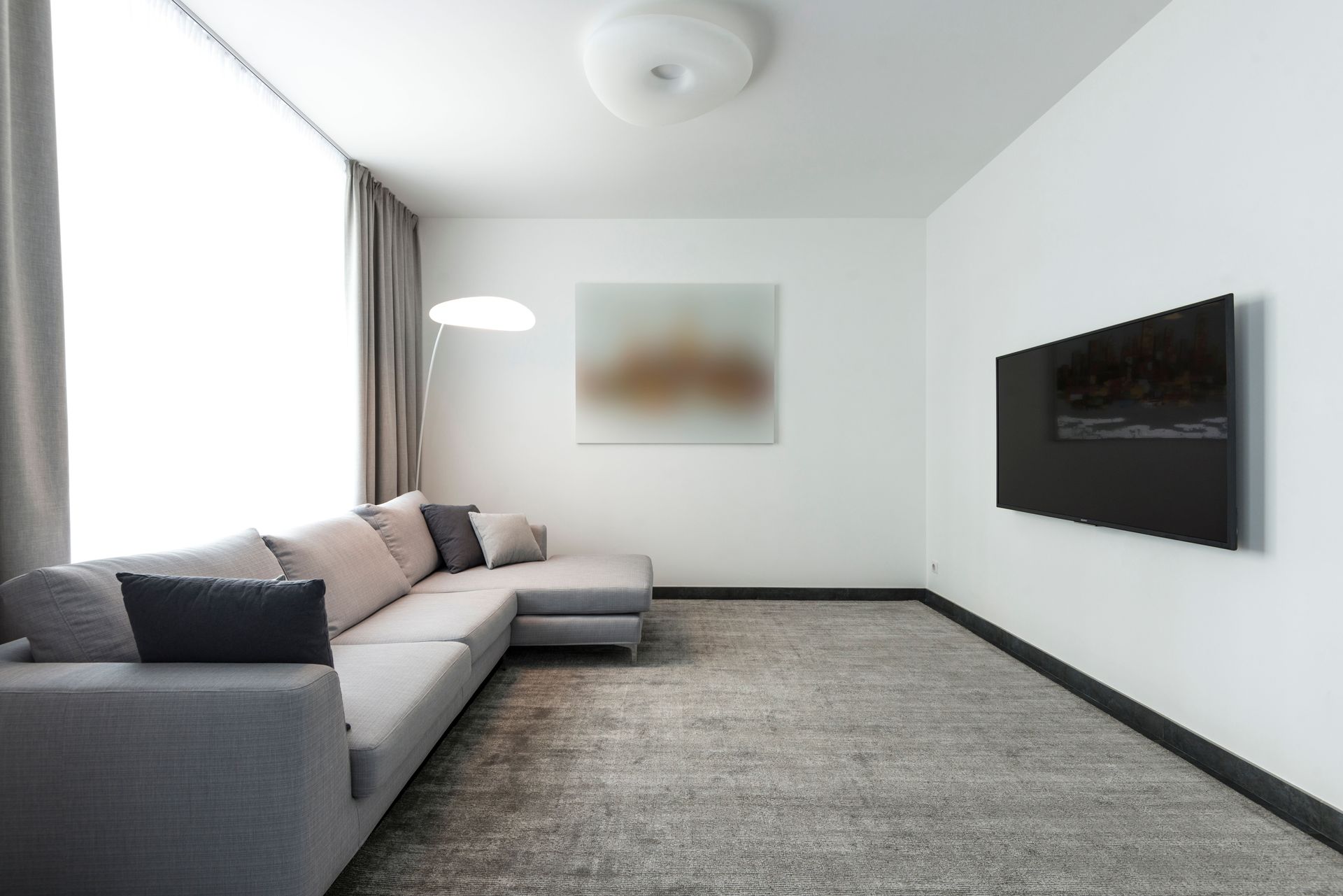 Modern living room with gray sectional sofa, wall-mounted TV, and large carpeted floor.