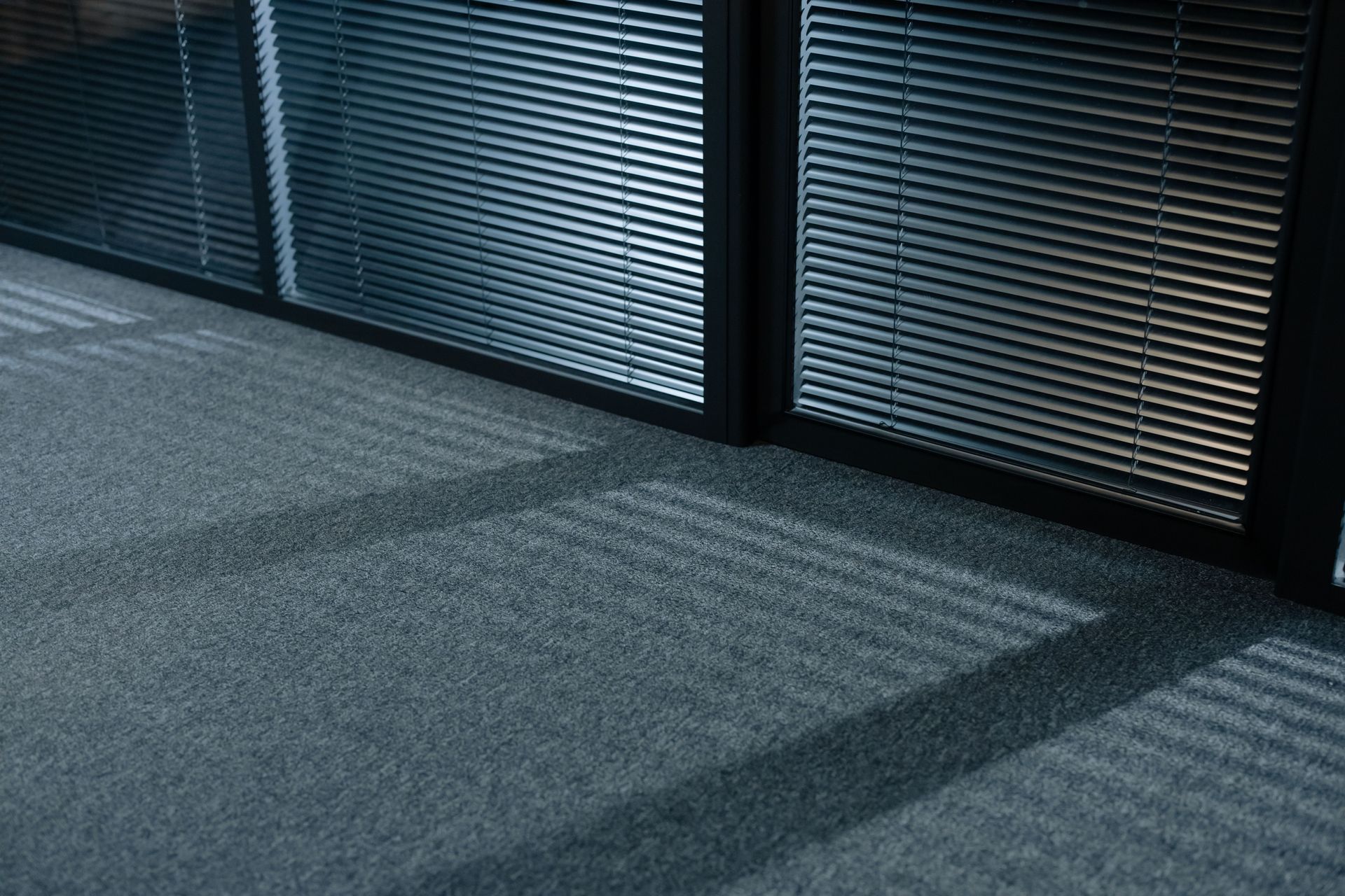 Sunlit office carpet with shadows from window blinds and glass wall panels