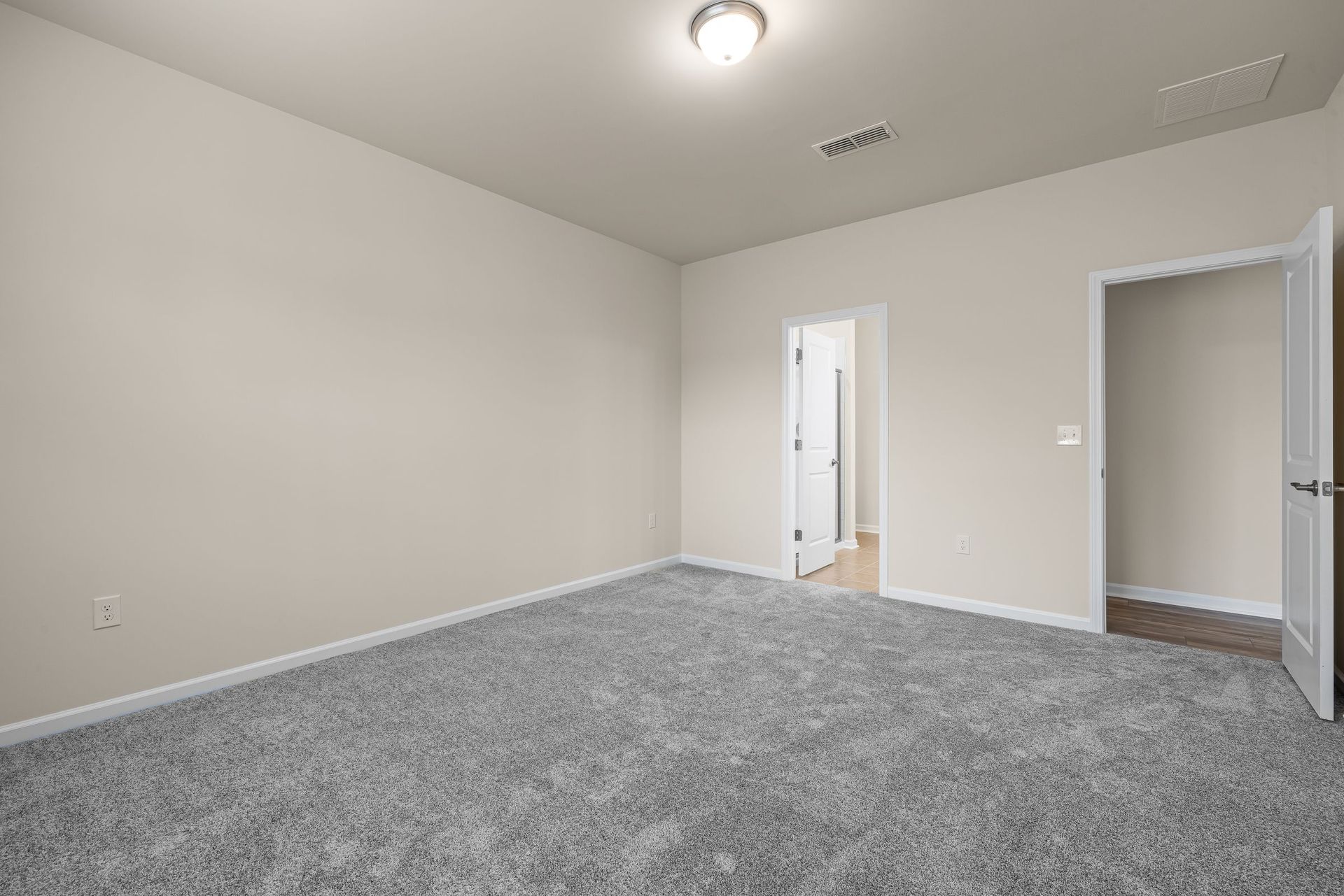 Empty room with new gray carpet and open doors leading to a hallway