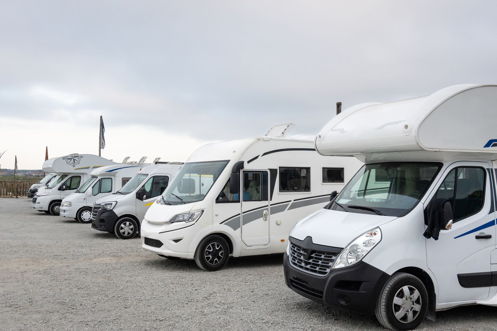 A row of white rvs are parked in a gravel lot.