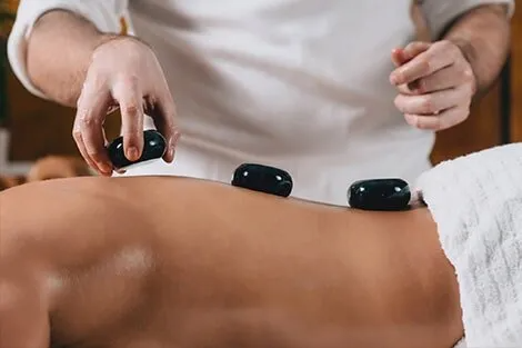 A man is giving a woman a hot stone massage.
