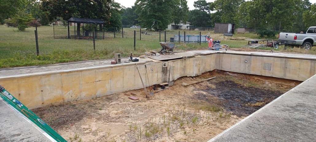 An empty, deteriorating rectangular swimming pool in a grassy outdoor setting.