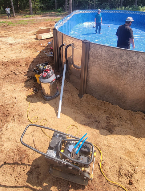 Construction of an above-ground pool. Men working inside, compactor and tools in the foreground.