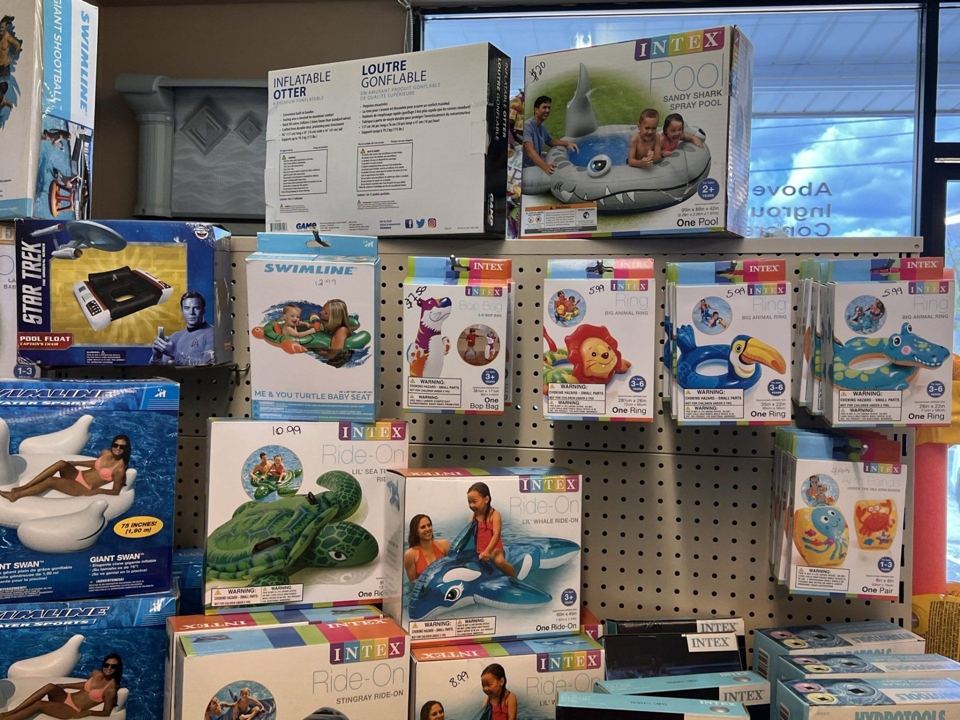 Shelves displaying various inflatable pool floats and toys, including animals and boats, inside a store.
