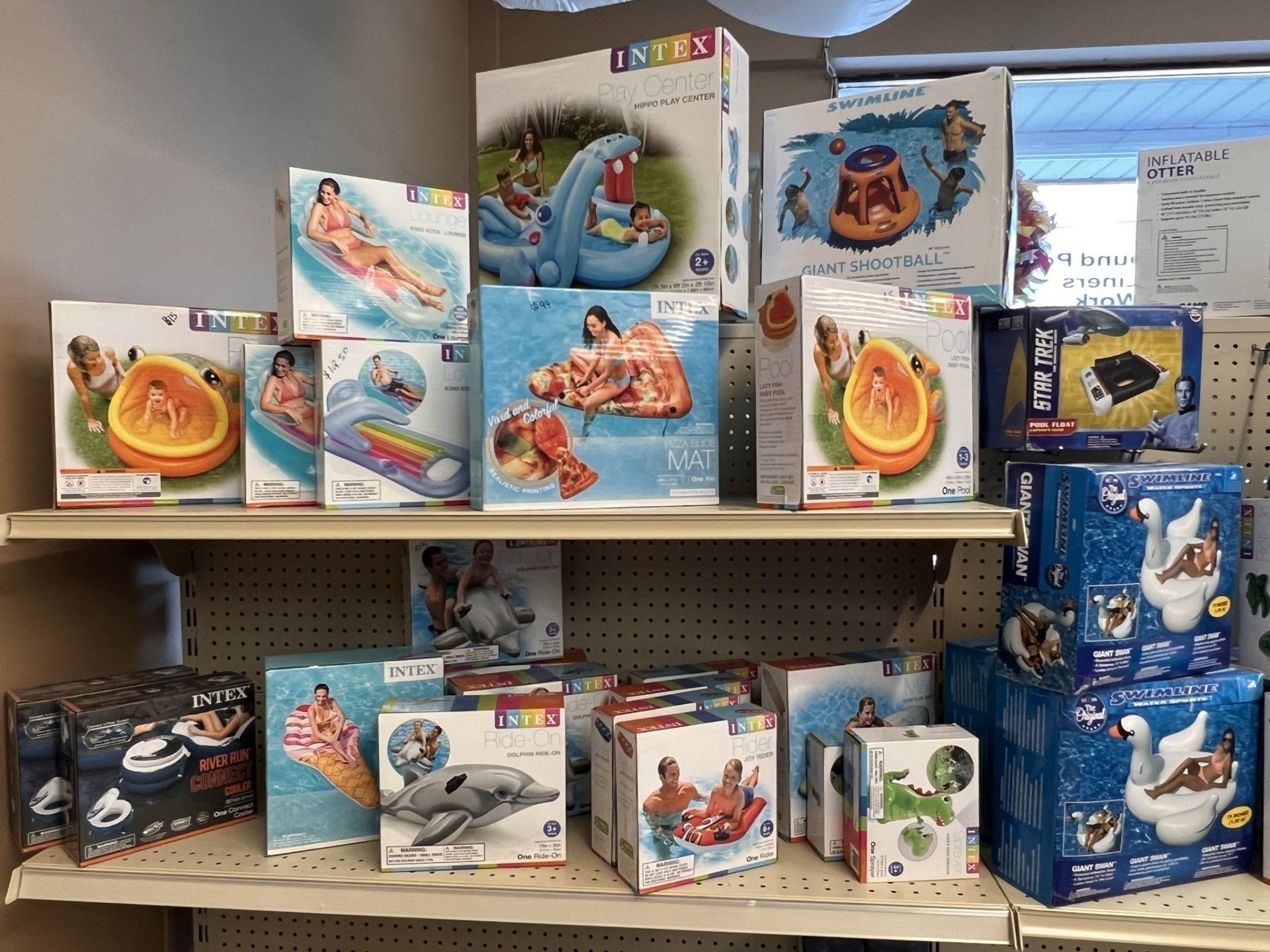 Shelves displaying various inflatable pool floats and toys in boxes.