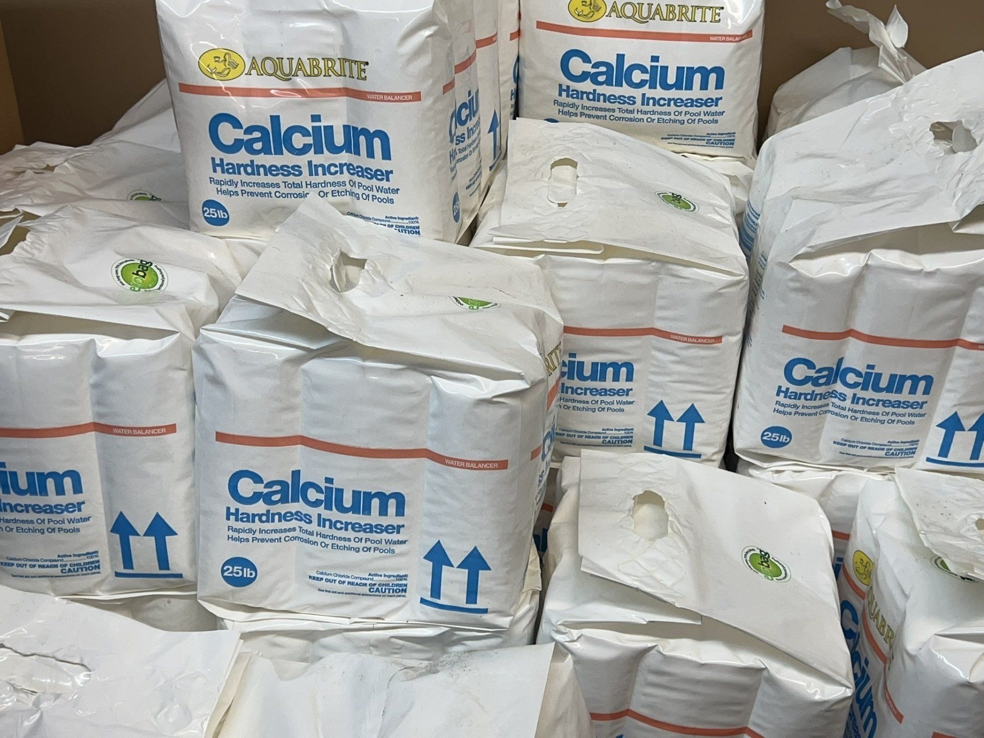 Bags of Aquarite Calcium Hardness Increaser piled in a box, with blue text and upward arrows.