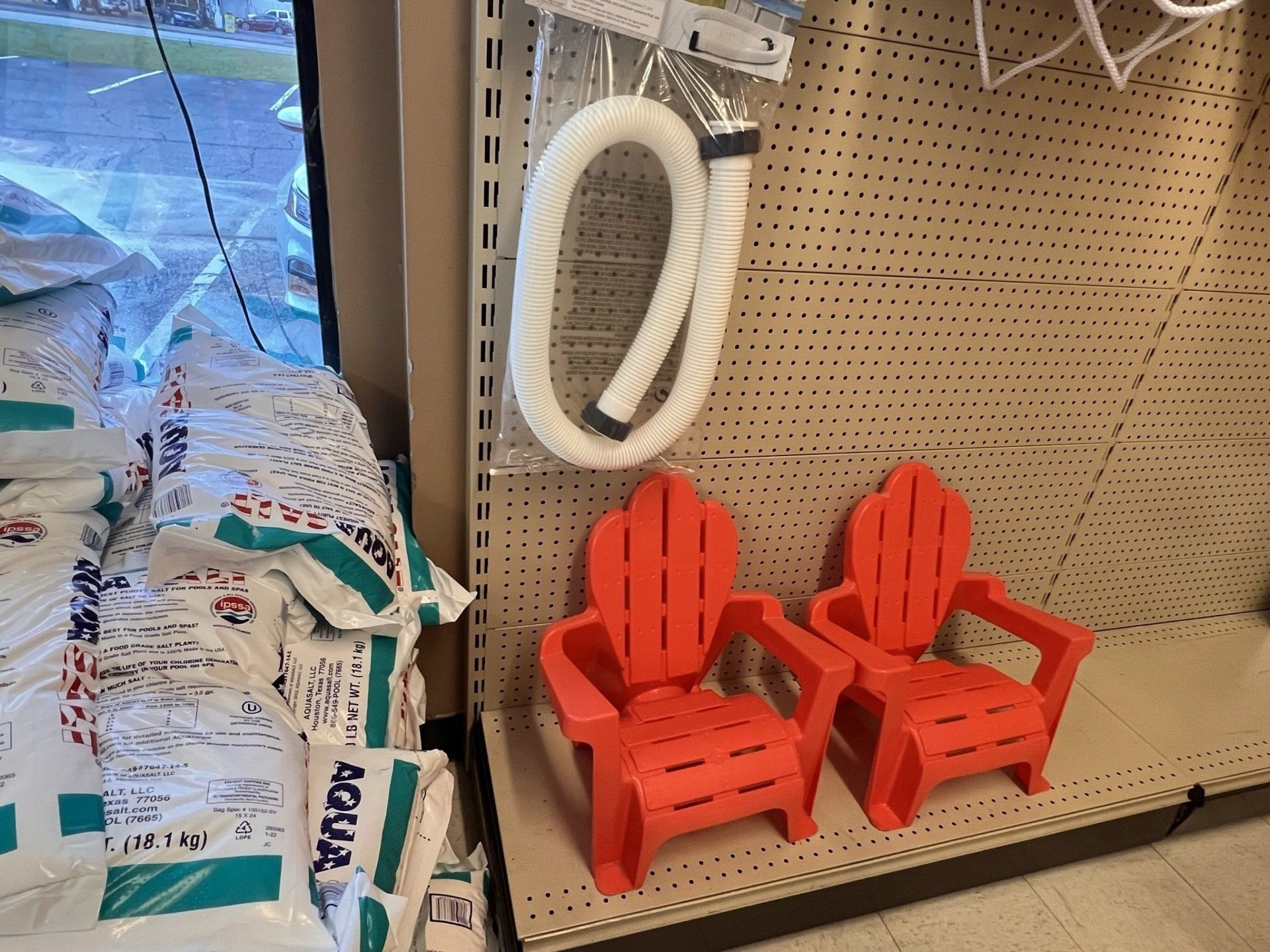 Two red plastic chairs and a white hose on a store shelf, bags of white powder on the left.