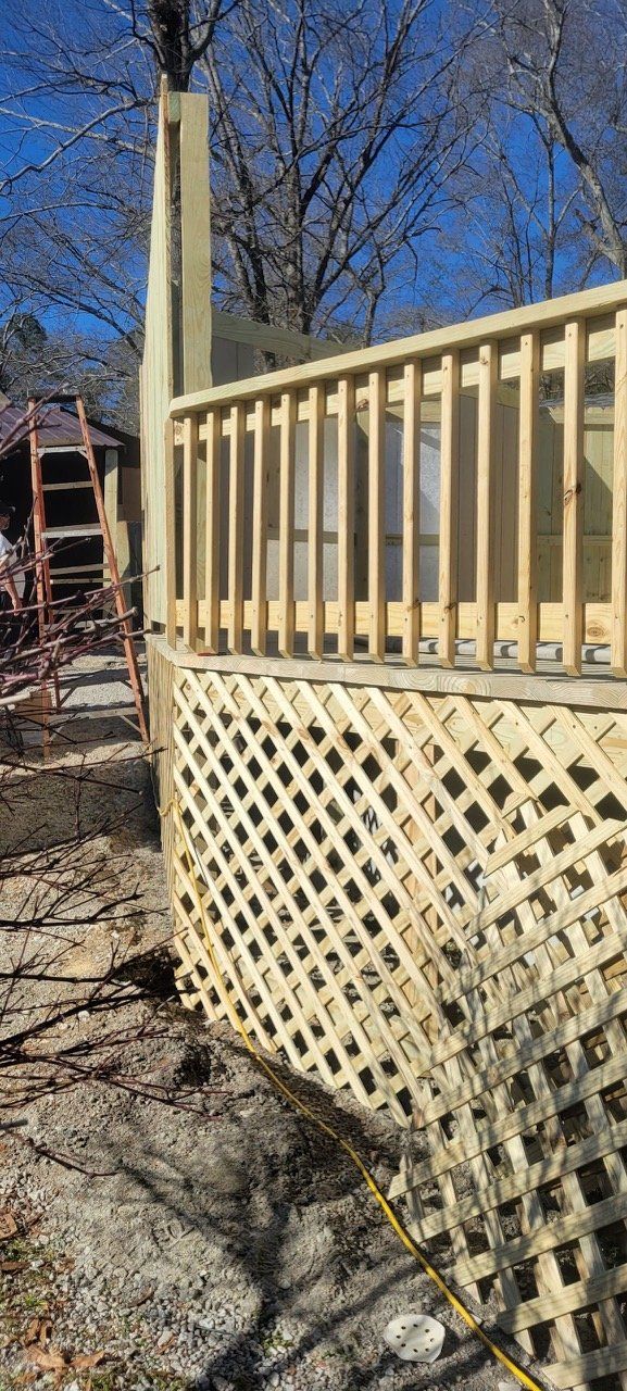 A partially constructed wooden deck with latticework base and railing against a backdrop of trees.