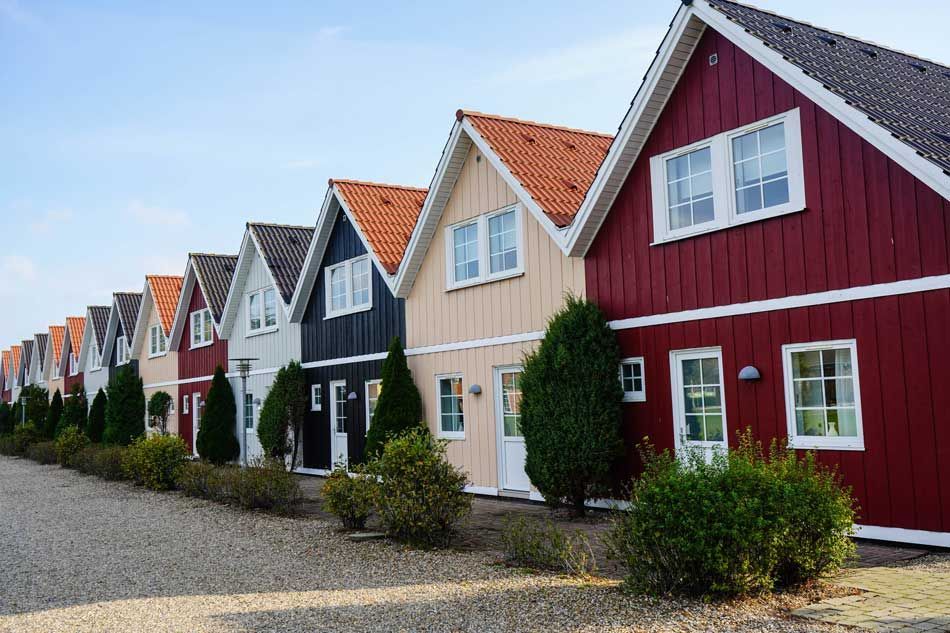 Row of colorful gable-fronted houses with red, beige, and black facades along a gravel road.