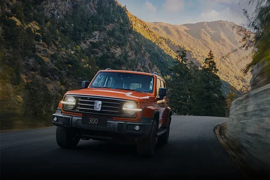 Un SUV naranja circula por una sinuosa carretera de montaña al anochecer.