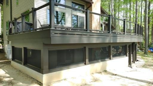 A sunlit wooden deck featuring an outdoor dining set next to a glass-walled structure overlooking a forested landscape. A sunlit wooden deck featuring an outdoor dining set next to a glass-walled structure overlooking a forested landscape.