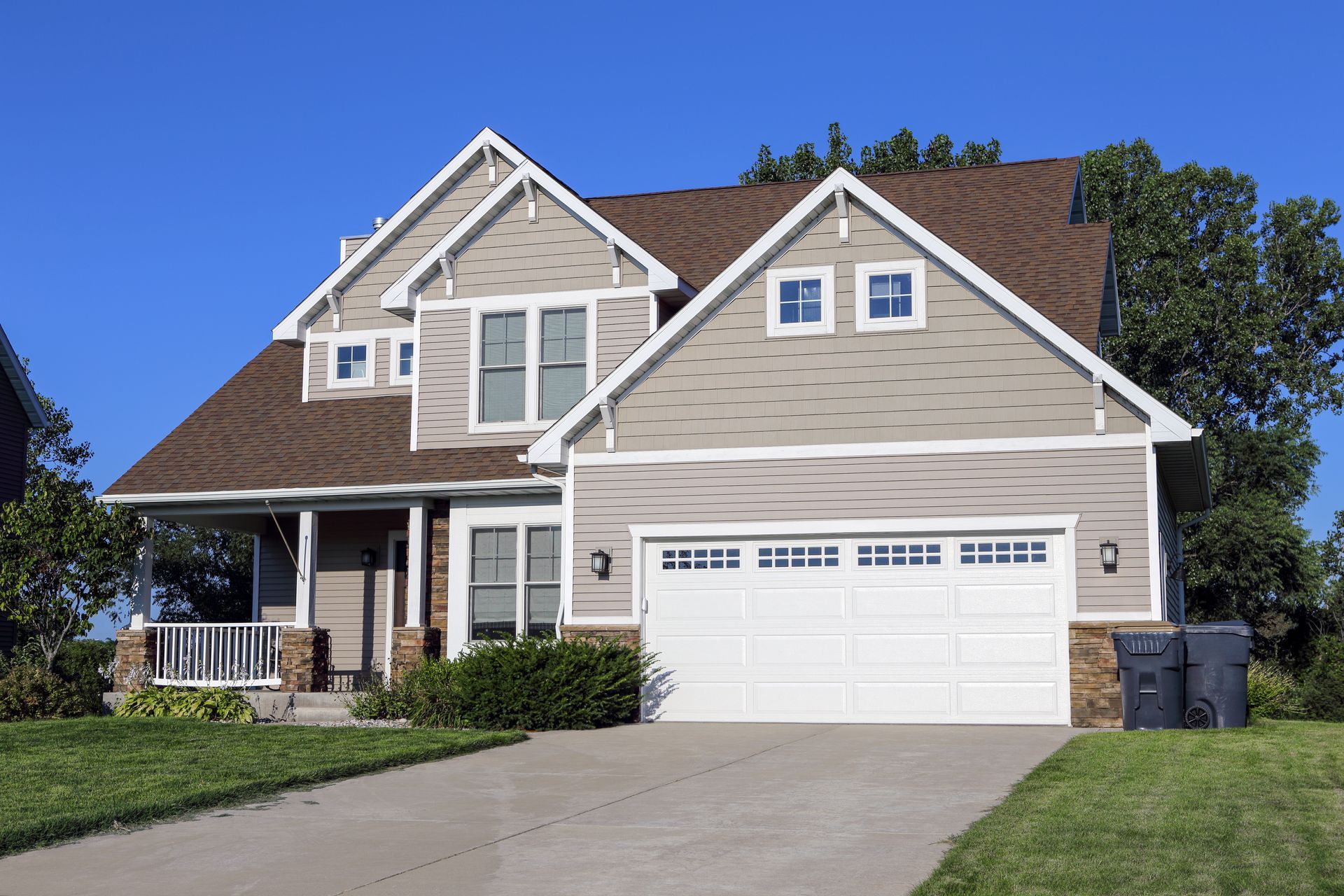 A two-story suburban house with light gray siding, brown shingles, and a white two-car garage on a clear, sunny day. A two-story suburban house with light gray siding, brown shingles, and a white two-car garage on a clear, sunny day.