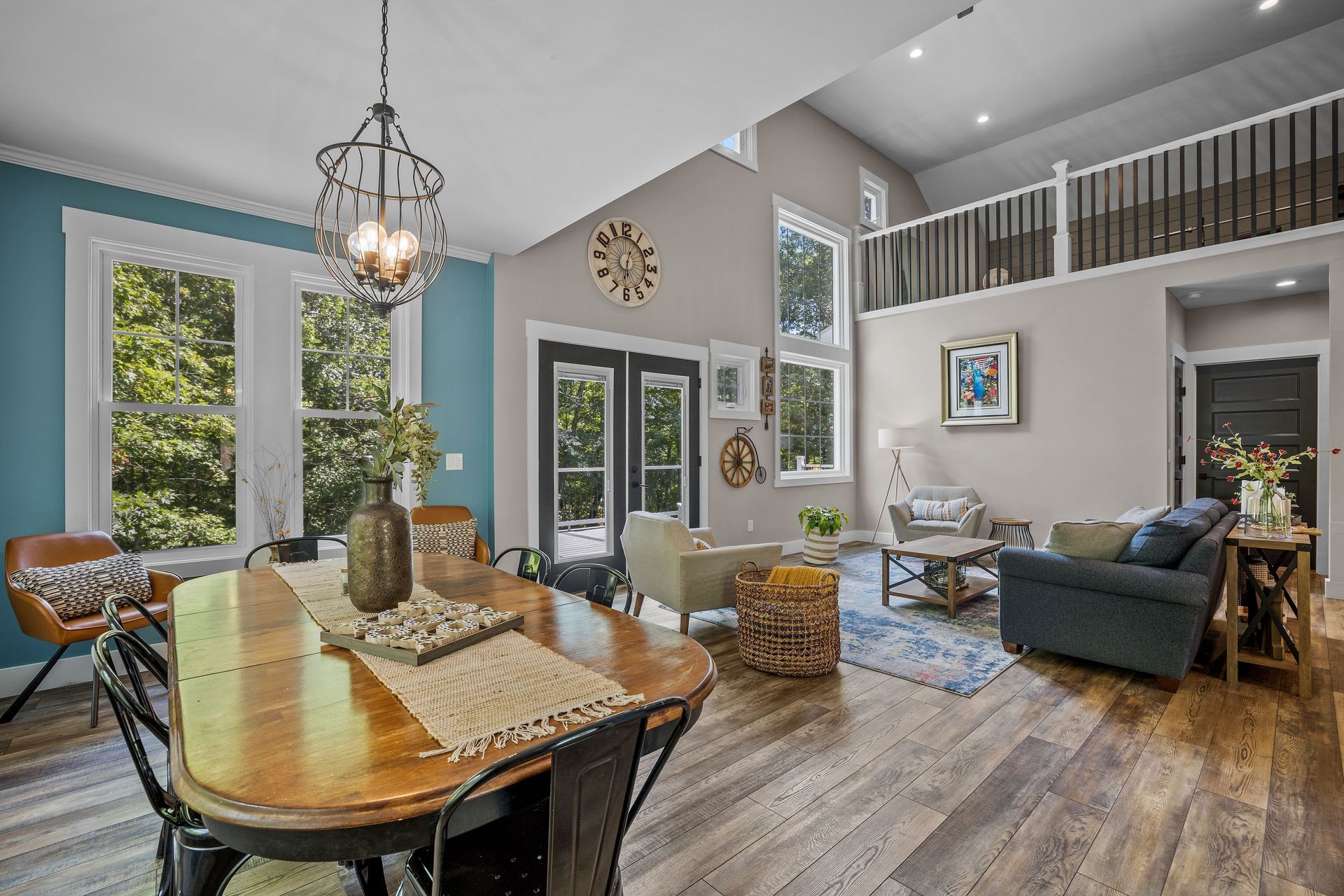 A bright living and dining room with high ceilings, wood floors, a wooden table, blue accent wall, and a loft overlook. A bright living and dining room with high ceilings, wood floors, a wooden table, blue accent wall, and a loft overlook.