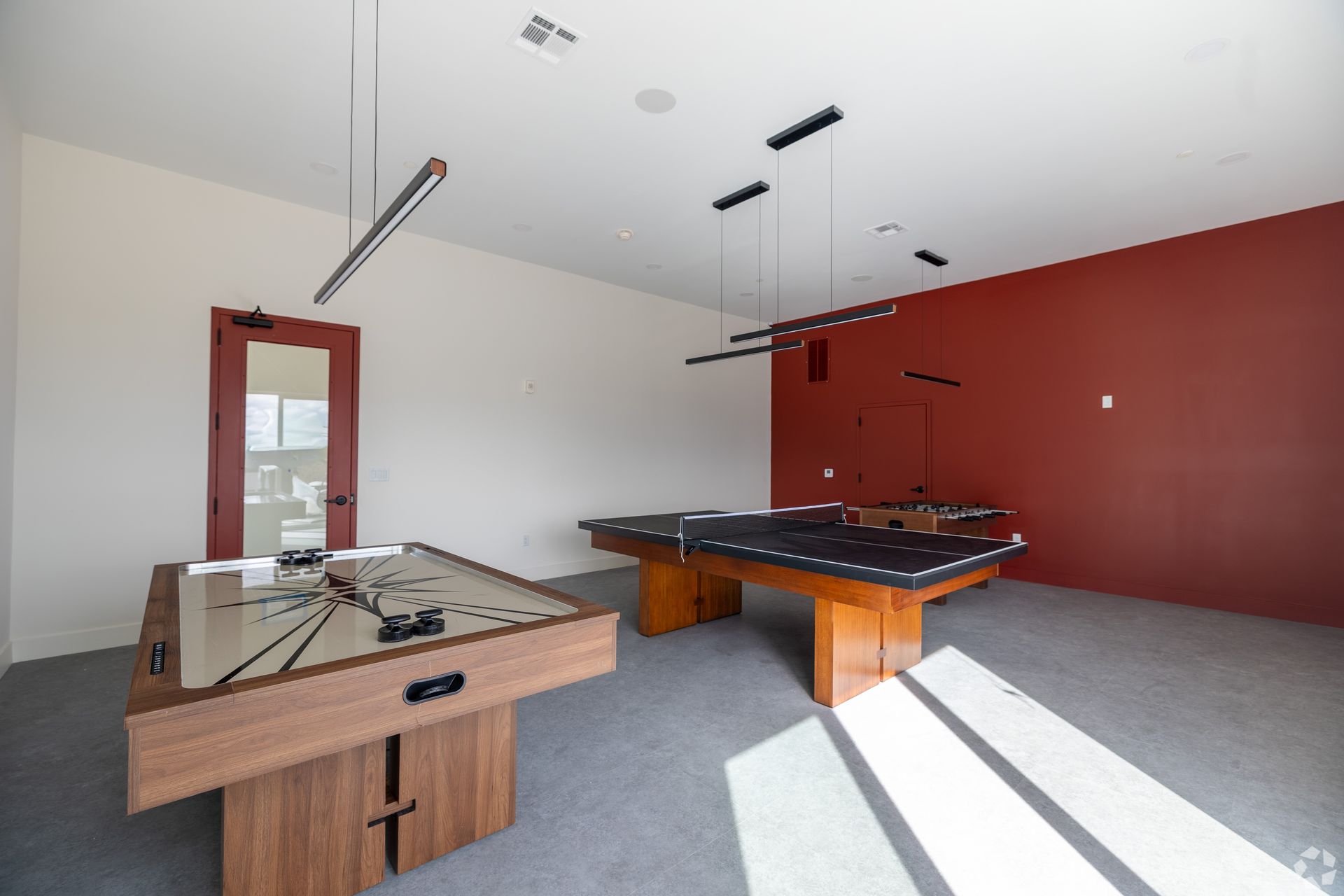Game room with shuffleboard and pool tables; red accent wall.