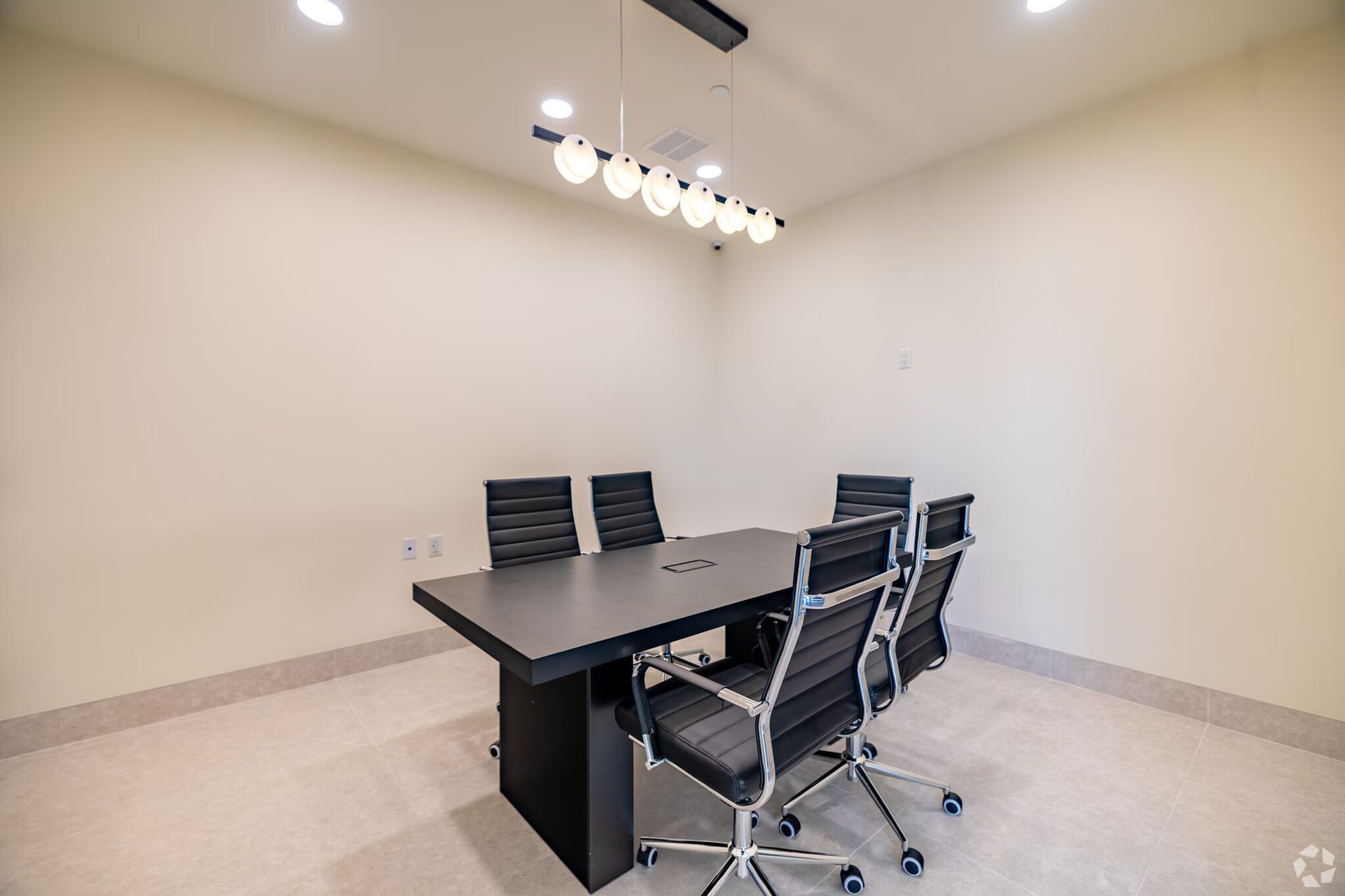 Conference room with a rectangular black table, six black rolling chairs, and a modern light fixture.