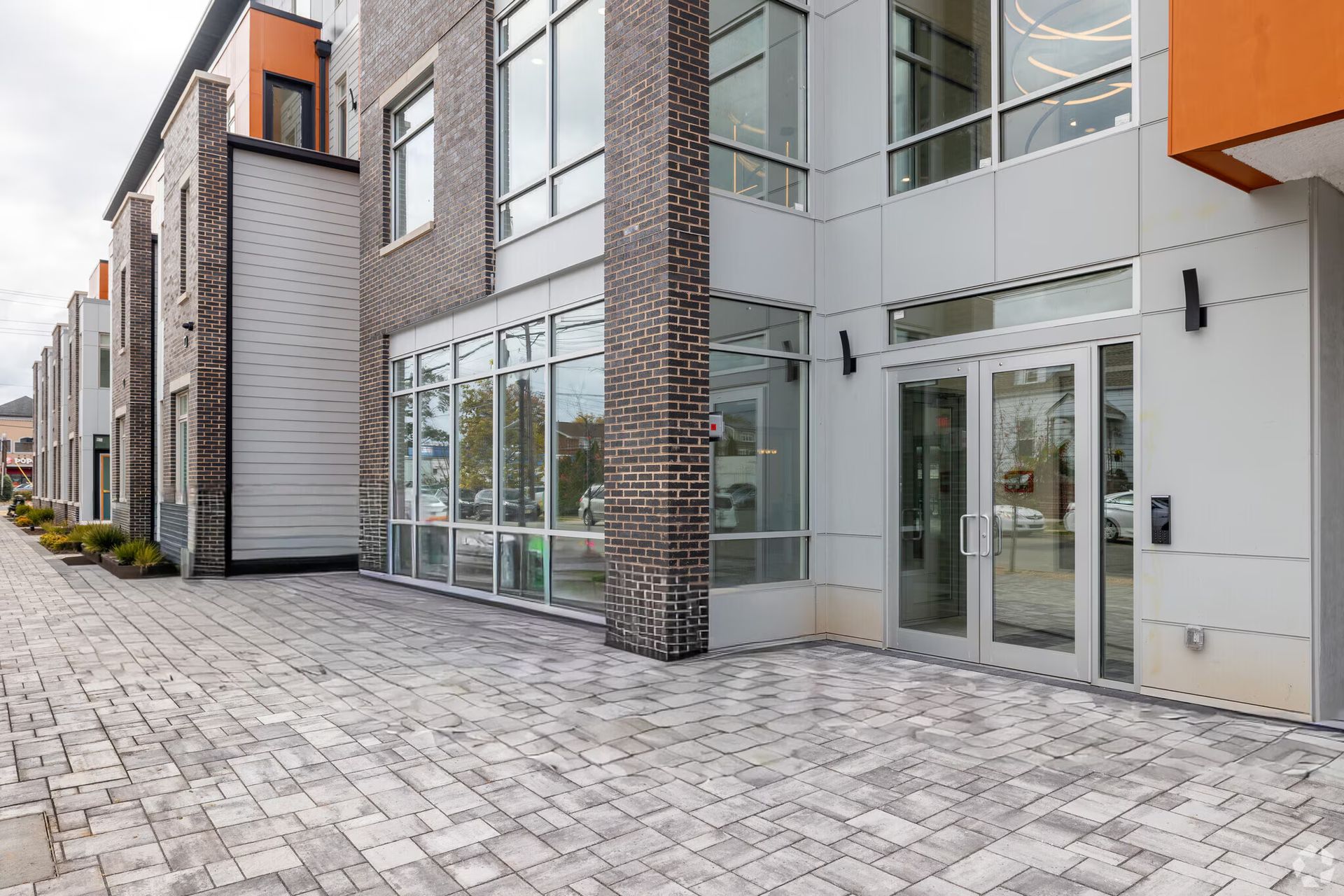 Building entrance with glass doors, large windows, brick columns, and a gray stone walkway.