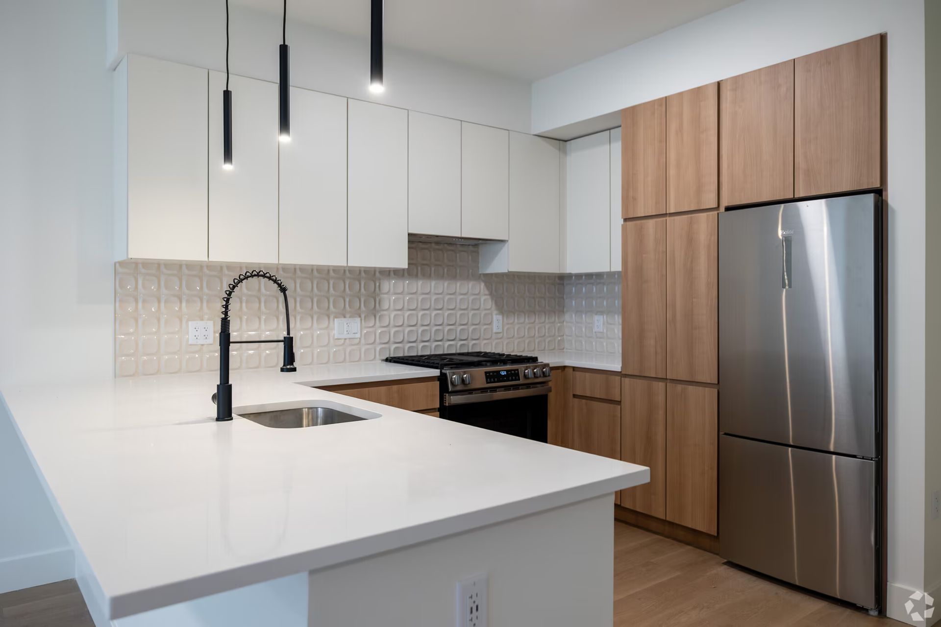 Modern kitchen with white countertops, stainless steel appliances, and wood cabinets.