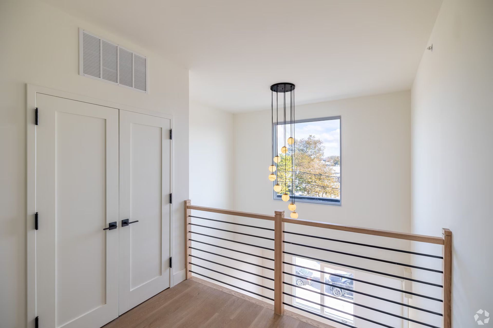 Hallway with white walls, doors, and a decorative light fixture over a railing.