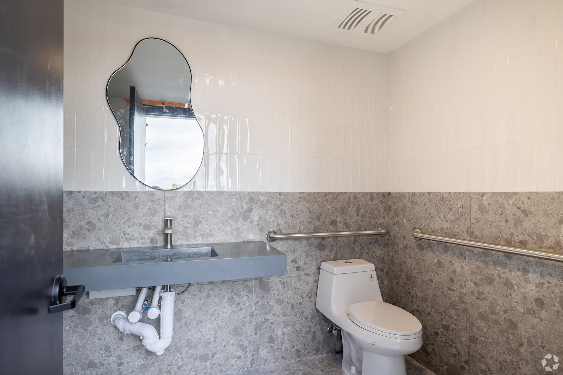 Accessible bathroom with stone walls, a floating sink, and grab bars.