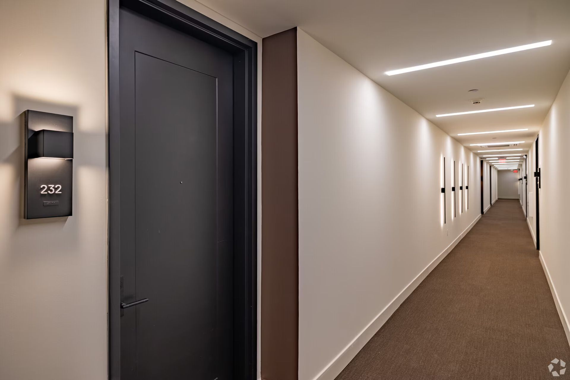 A long, modern hallway with carpet and several doors on the right. Door 232 on the left.