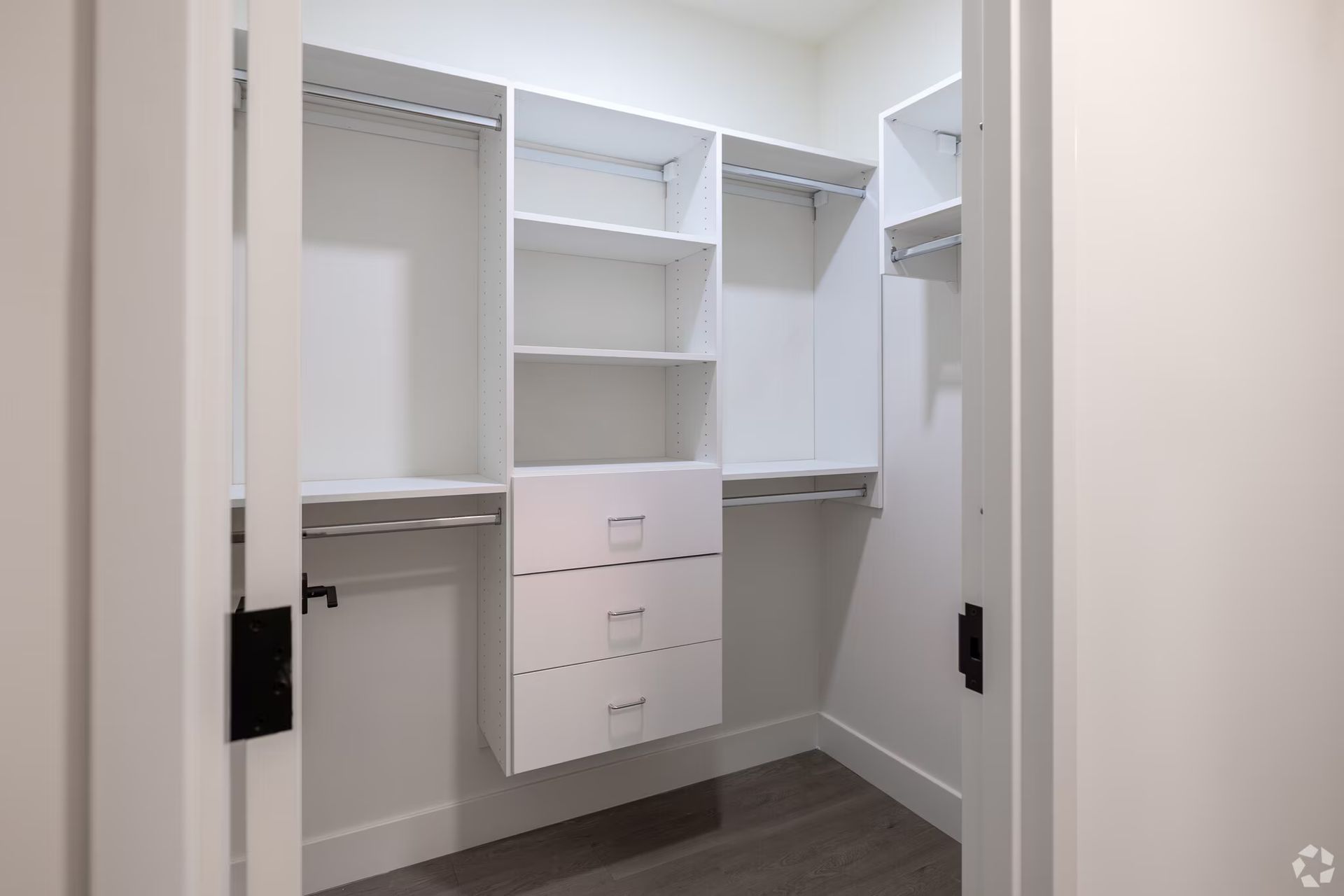 White walk-in closet with built-in shelves, drawers, and hanging rods. Light wood floor, white walls and trim.