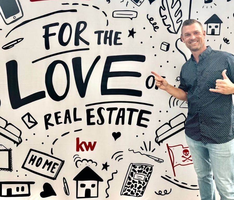 Man standing beside a mural reading “For the Love of Real Estate” with house doodles