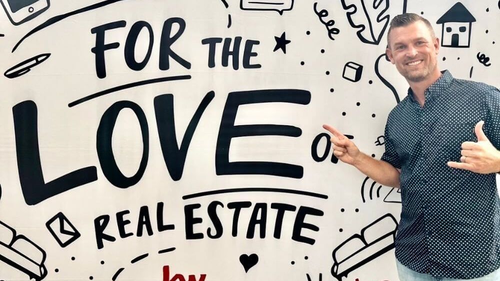 Man standing beside a white board with bold text reading “For the Love of Real Estate.”