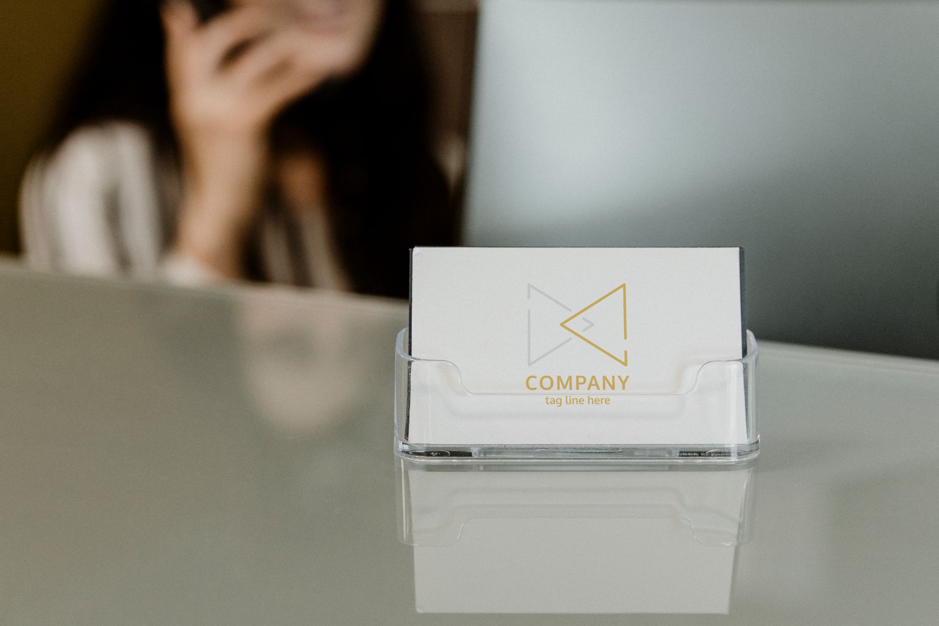 Business cards displayed in a clear acrylic holder on a desk with a blurred person in the background