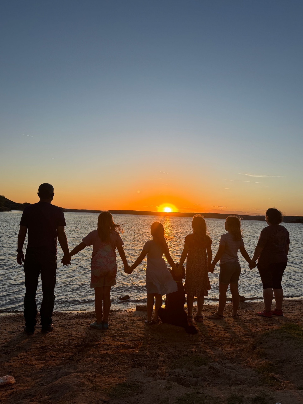 Through it all, together Family of six holding hands in silhouette while watching a sunset over the water
