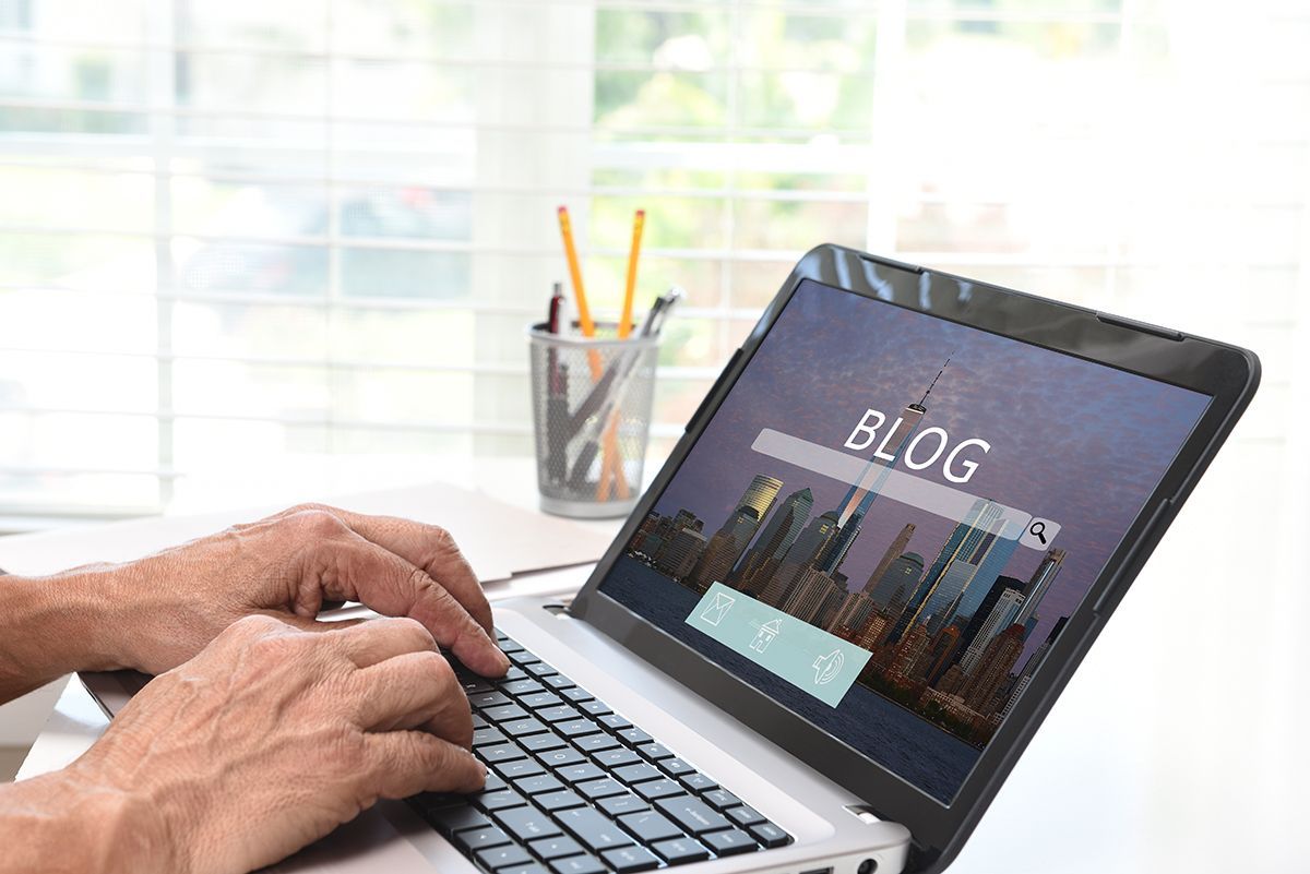 Every post is a new door for search engines to find you Hands typing on a laptop with a blog homepage displayed on the screen