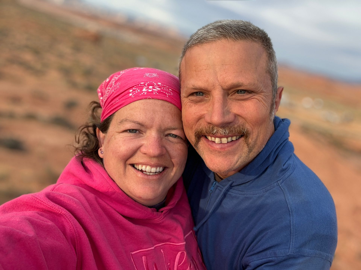Jennifer and Phil, the team behind Designs On The Go Jennifer and Phil, owners of Designs On The Go, smiling together in front of a desert landscape
