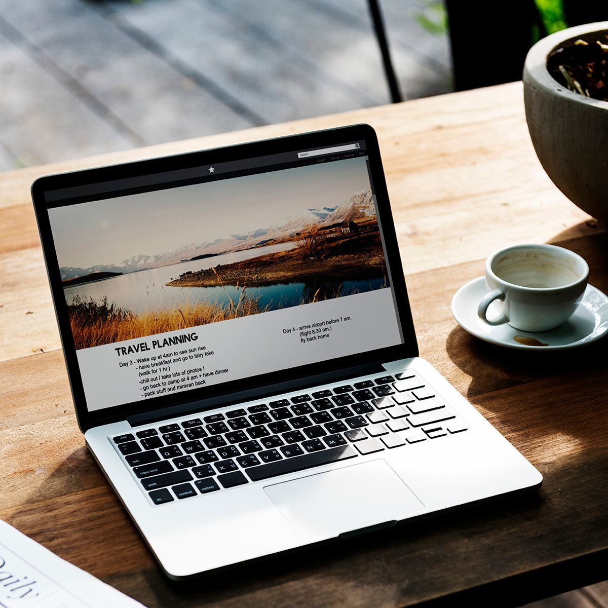 Laptop on a wooden table displaying a travel planning website with a mountain lake landscape