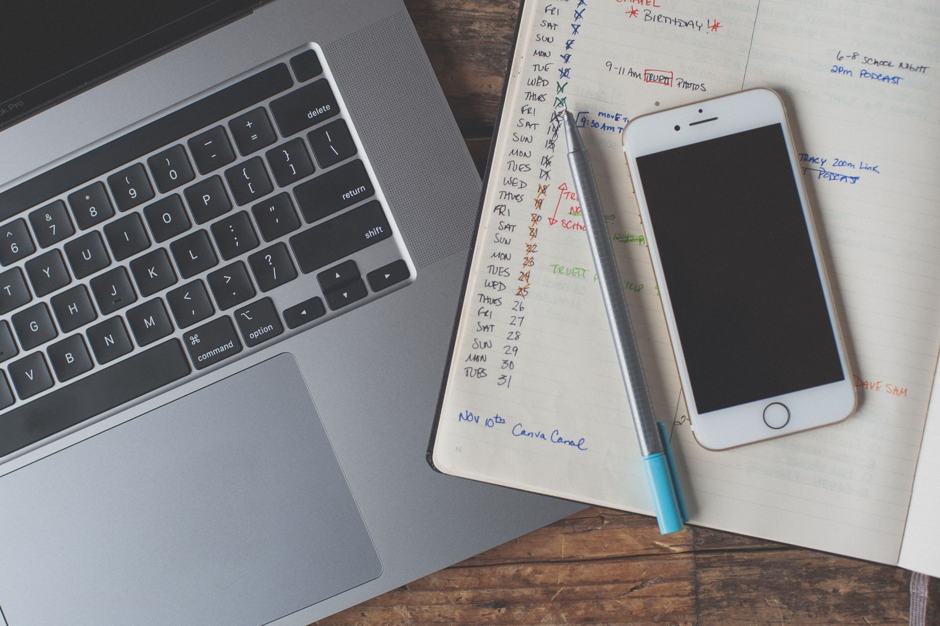 Laptop, notebook planner, and smartphone on a desk with a pen.